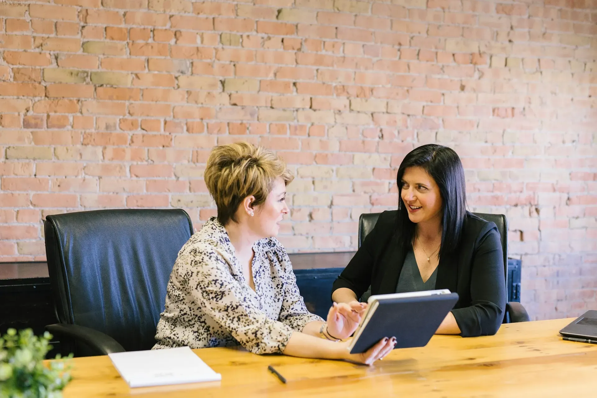 Two women talking over a tablet at a meeting table